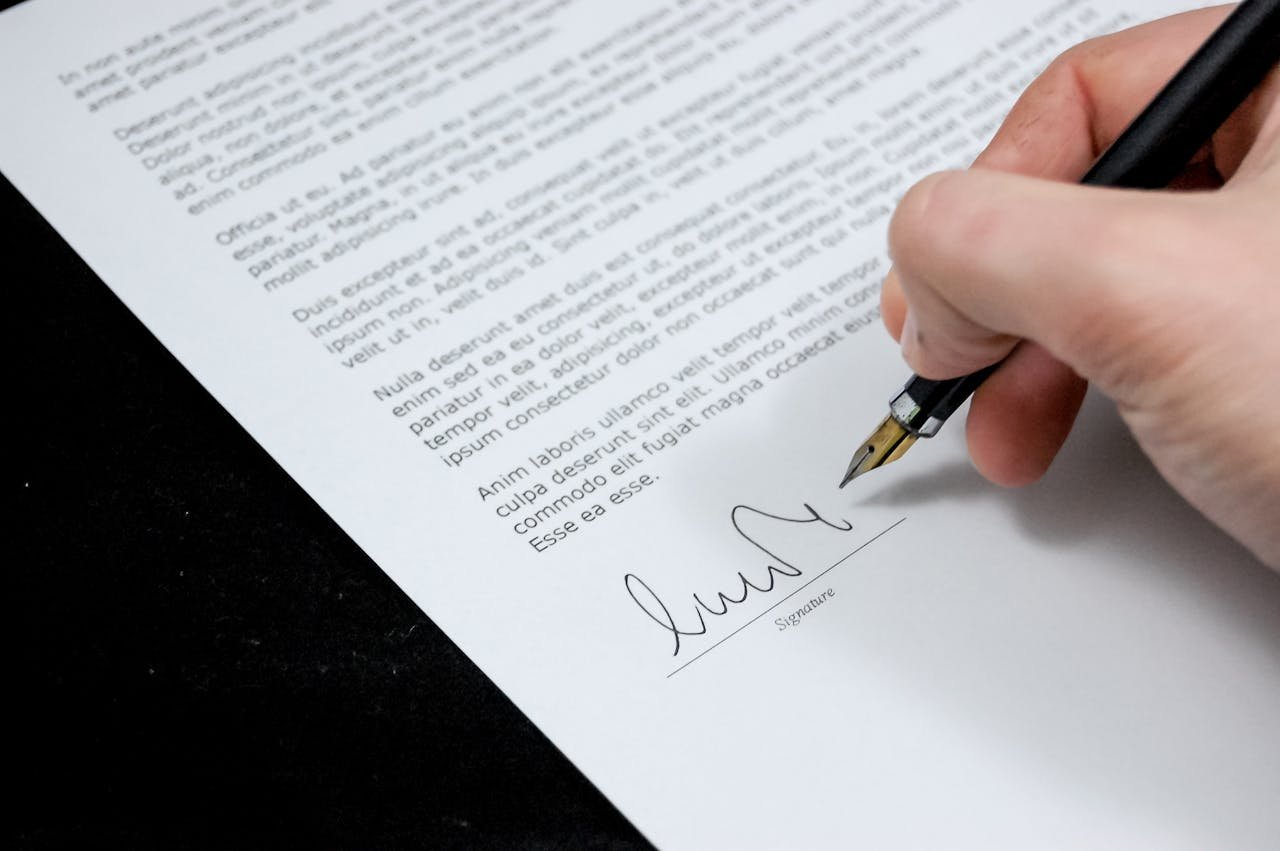 Close-up of a hand signing a formal document with a fountain pen, indicating agreement.