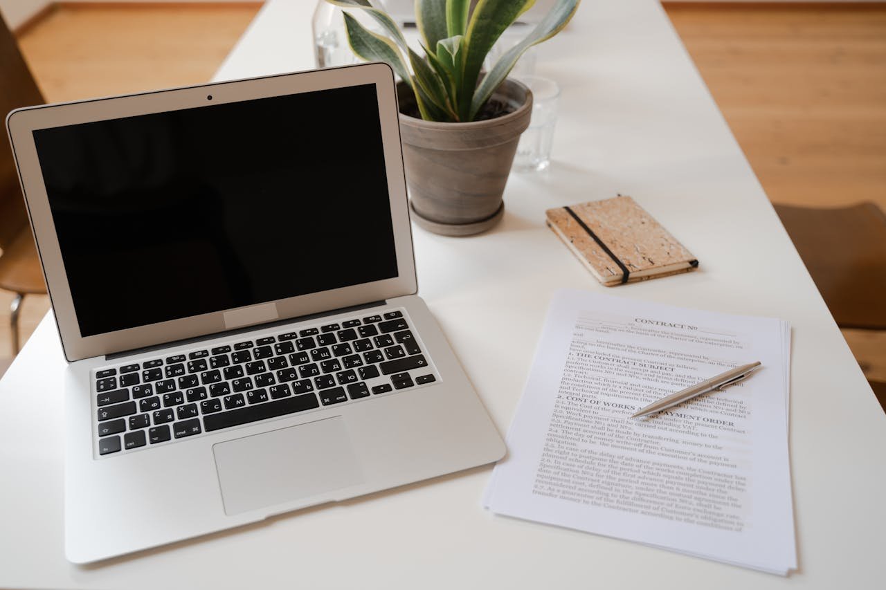 A serene office desk setup featuring a laptop, plant, and contract document ideal for business themes.