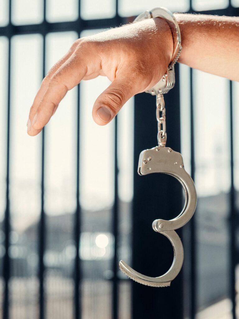 Hand grasping open handcuff with prison bars behind, symbolizing crime and justice.