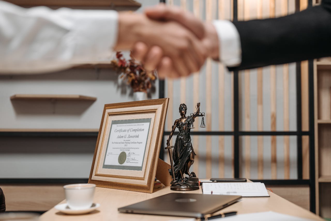 A professional handshake in an office with diploma and Lady Justice statue, symbolizing law and achievement.